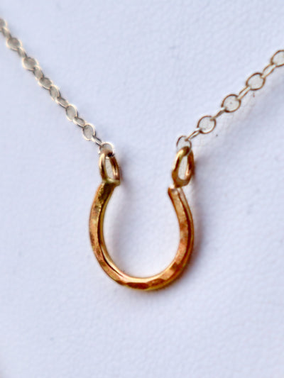 Silver and Gold Mini Lucky Horseshoe Charm Necklace features a 16 gauge gold-fill horseshoe that is lightly hammered and measures approx. 1/2" in length. The necklace features an adjustable 16-18 inch sterling silver chain.
